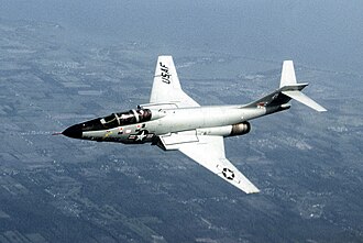 ภาพถ่ายเครื่องบิน F-101 กำลังบิน ด้านข้างลำตัวเครื่องบินมีสัญลักษณ์รูปดาว ด้านซ้ายของสัญลักษณ์มีข้อความว่า กองทัพอากาศสหรัฐฯ แพนหางระดับของเครื่องบินอยู่ด้านบนของครีบหาง