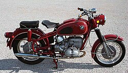 รถจักรยานยนต์ BMW R69US สีแดง จอดอยู่บนพื้นกรวด/คอนกรีต