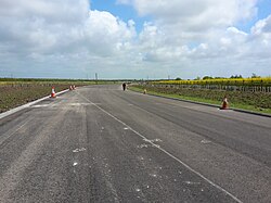 A picture of a paved, partly-complete A5758 road without any markings on its pavement and with traffic cones lining its sides
