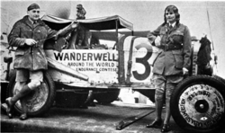 ชายและหญิงผิวขาว ยืนอยู่หน้ารถยนต์ฟอร์ดที่ทาสีด้วยคำว่า "Wanderwell การแข่งขันความอดทนรอบโลก" ทั้งคู่สวมเสื้อผ้าแบบเดียวกัน