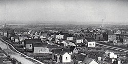 ภาพถ่ายบริษัท Elcor ในราวปี 1916 แสดงให้เห็นทางเดินไม้กระดาน รั้วไม้กระดาน 4 ด้าน และการติดตั้งสายส่งไฟฟ้า