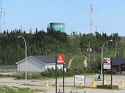 ภาพถ่ายแสดงให้เห็นลานจอดรถในพื้นที่กึ่งชนบท ด้านหน้ามีป้ายเขียนว่า Tim Hortons, Service Canada และ Labrador Mall ส่วนด้านหลังเป็นอาคารอุตสาหกรรมขนาดใหญ่ที่มีคำว่า Labrador City เขียนอยู่