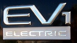 ป้ายโลโก้มีข้อความ "EV1" เป็นตัวอักษรขนาดใหญ่ สีเมทัลลิก และมีสไตล์ ด้านล่างมีคำว่า "ELECTRIC" เป็นตัวอักษรพิมพ์ใหญ่ขนาดเล็กกว่า สีขาว