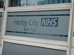 หน้าต่างกระจกฝ้าบางส่วน มีข้อความว่า 'Holby City NHS, NHS Trust'